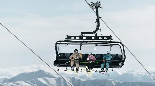 Skiers in chairlift in front of snowy mountain landscape