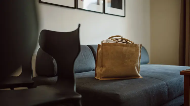 Sac en tissu marron sur un canapé bleu, chaise noire au premier plan, photos au mur
