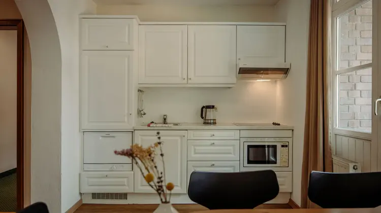 Petite kitchenette avec placards blancs, évier, micro-ondes et bouilloire électrique