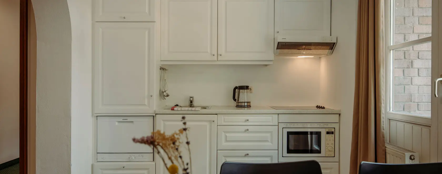 Petite kitchenette avec placards blancs, évier, micro-ondes et bouilloire électrique