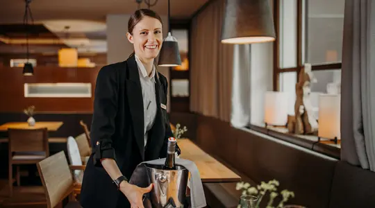 Frau im Service hält Weinkühler mit Flasche und lächelt
