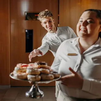 Zwei Personen mit Donuts auf einem Tablett lächeln