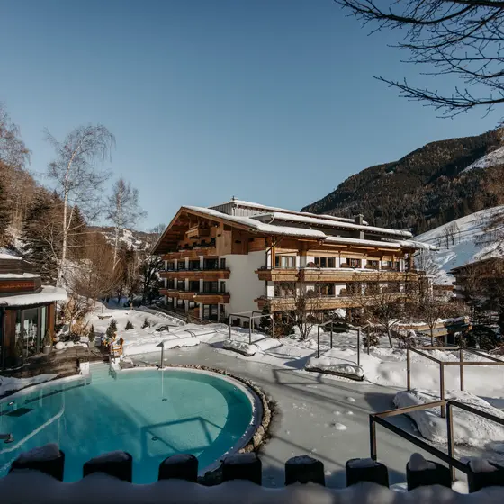 Beheizter Außenpool des Gartenhotel Theresia mit Dampf und Schnee vor Bergkulisse