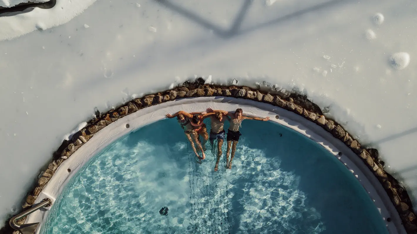 Vier Personen liegen im Pool, umgeben von Schnee