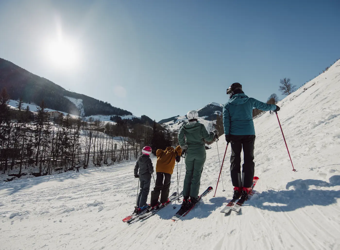 Familie fährt Ski an einem sonnigen Wintertag einen Hang hinunter