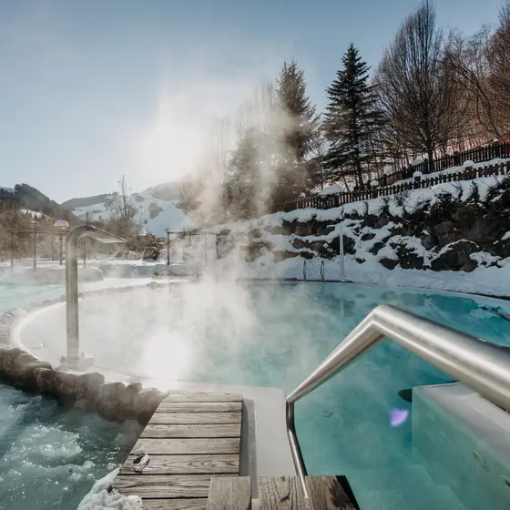 Beheizter Außenpool des Gartenhotel Theresia mit Dampf und Schnee vor Bergkulisse