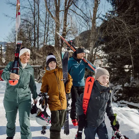 Familie mit Skiern und Skischuhen geht im Winter durch eine verschneite Landschaft