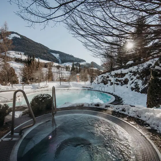 Beheizter Außenpool des Gartenhotel Theresia mit Dampf und Schnee vor Bergkulisse