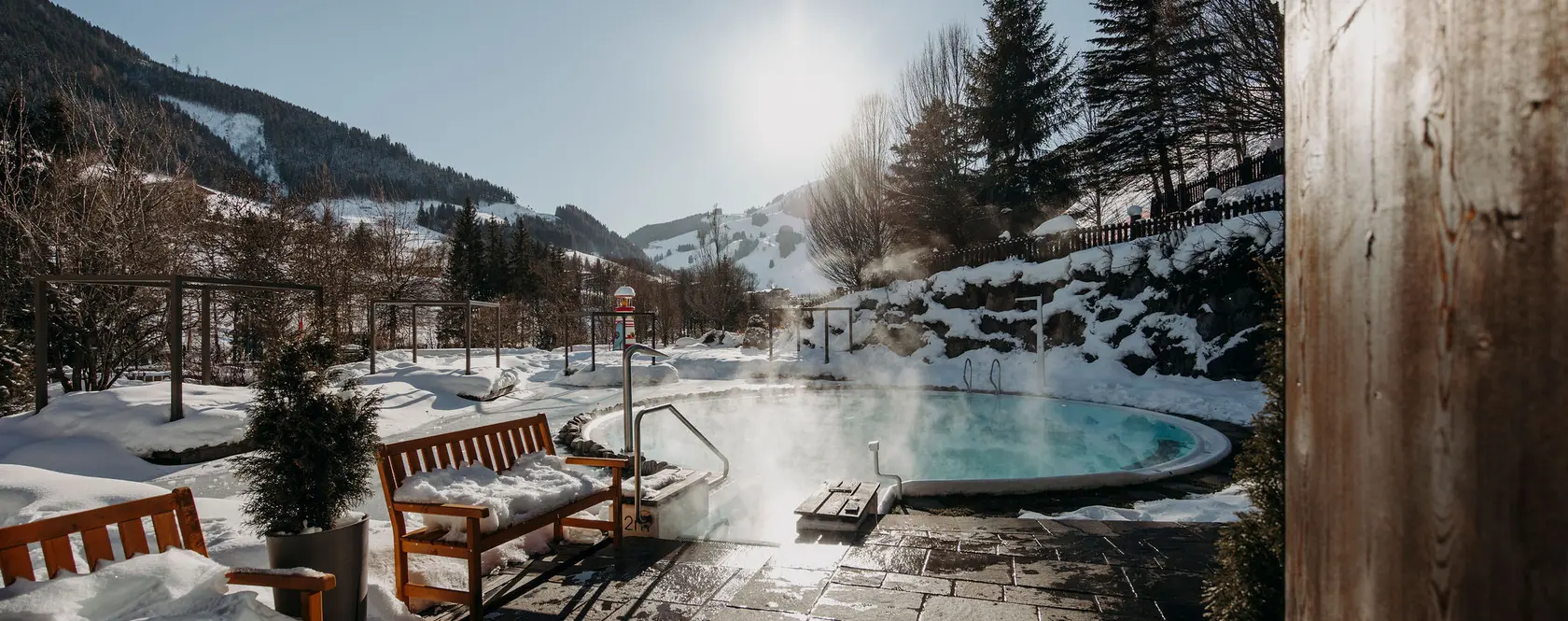 Beheizter Außenpool des Gartenhotel Theresia mit Dampf und Schnee vor Bergkulisse