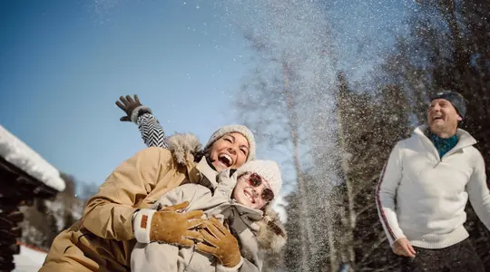 Woman and child in the snow, laughing, with hats and winter clothes, throwing snowballs
