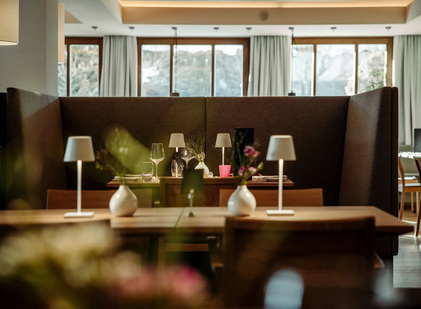 Restaurant mit Tischen, Lampen, Blumen und Fenstern im Hintergrund