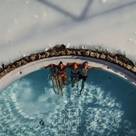 Vier Personen entspannen im Pool, umgeben von Schnee