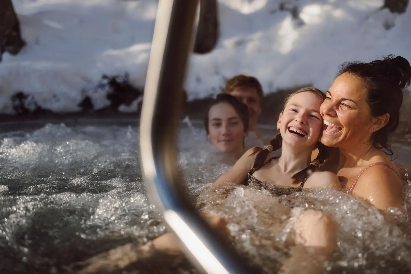 Lachende Menschen im warmen Wasser vor verschneiter Bergkulisse