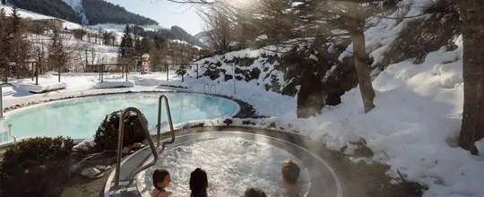 Winterlandschaft mit dampfendem Whirlpool und Badenden im Vordergrund