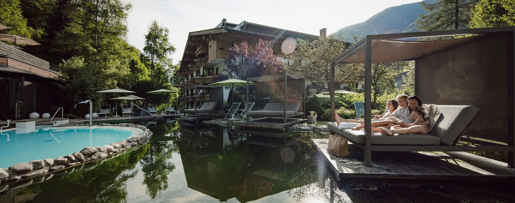 Eltern mit zwei Kindern am Hotelbadeteich in Saalbach