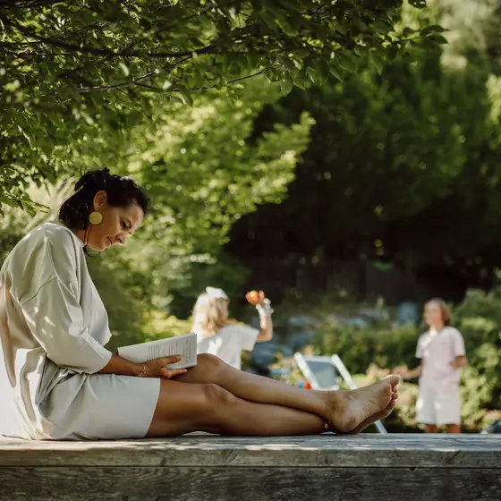 Woman reading a book in the garden while her two children play in the garden