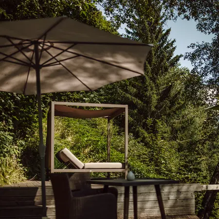 Gartenmöbel mit Liege unter Sonnenschirm vor grüner Vegetation