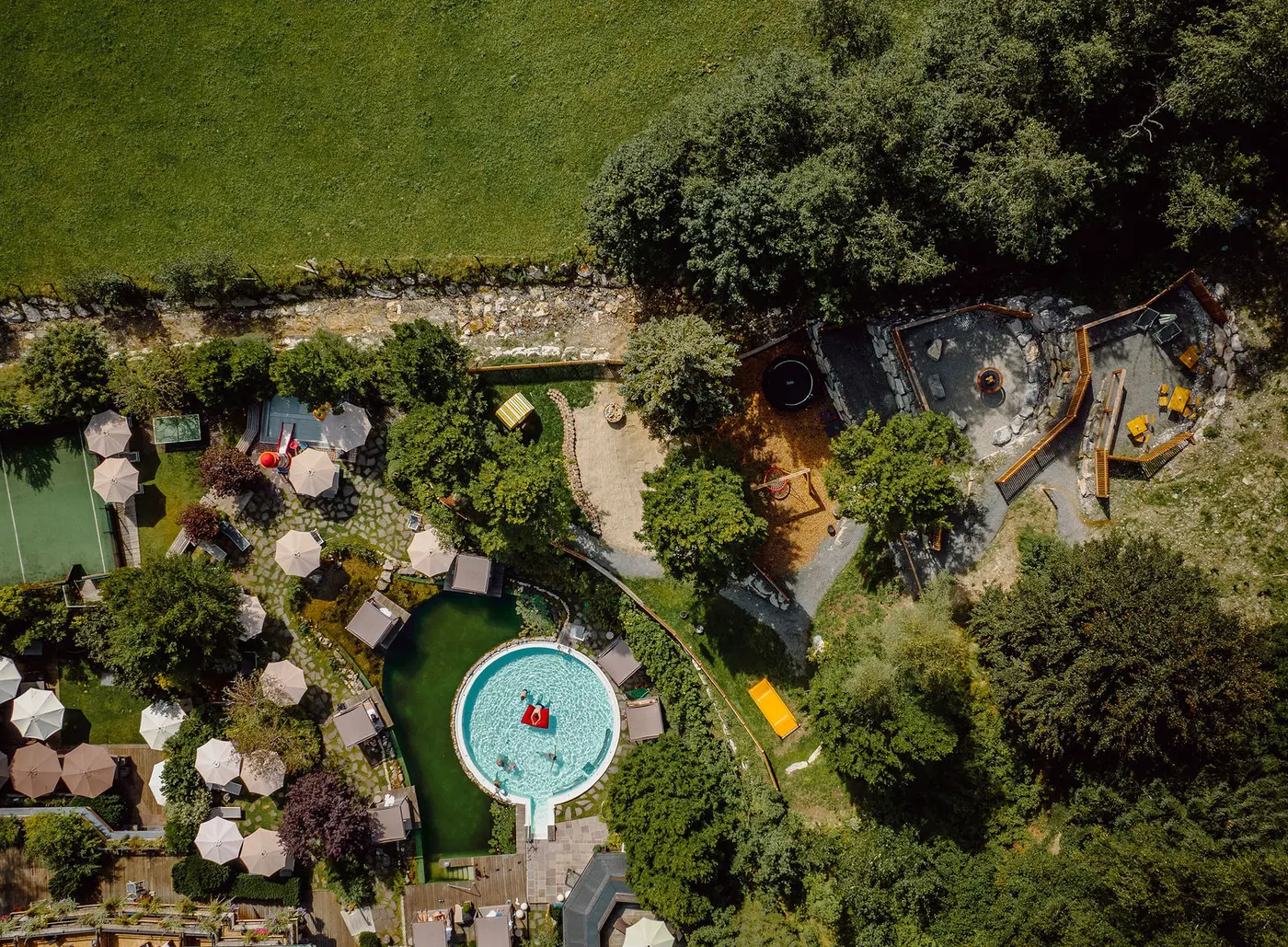 Luftaufnahme von Poolanlage mit Liegen, Spielplatz und Grünflächen umgeben von Bäumen