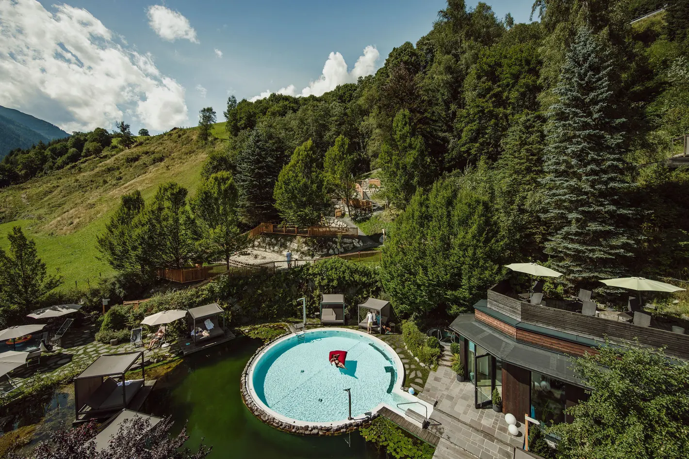 Rundes Schwimmbad in grüner Landschaft mit Bäumen und Hügeln