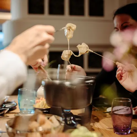 Personen essen Käsefondue mit Brot und Gemüse am Tisch