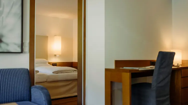 Hotelzimmer mit Bett, Schreibtisch und Sessel durch Türrahmen gesehen