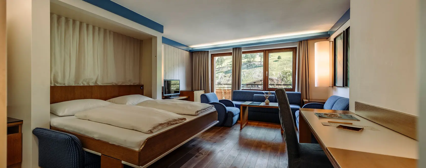 Hotelzimmer mit Doppelbett, Sitzecke und Schreibtisch vor Fenster mit Bergblick