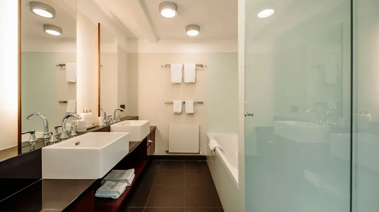 Salle de bain lumineuse avec deux lavabos, baignoire et serviettes