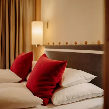 Bett mit roten Kissen und weißen Laken vor Wand mit Lampe