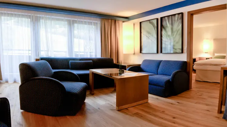 Blauer Wohnbereich mit Sofa, Sessel, Tisch, Bildern und hellem Holzfußboden