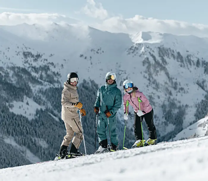 Three skiers in winter clothing in front of a snowy mountain landscape